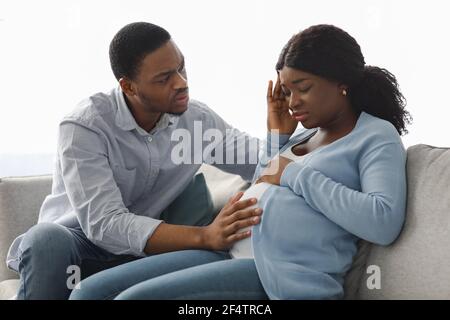 Schwarze schwangere Dame, die sich krank fühlt, besorgter Ehemann, der neben ihr sitzt Stockfoto