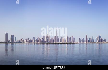 Dubai Downtown Skyline Panorama mit Reflexionen in Dubai Creek, kalte Farben, von der Dubai Creek Hafenpromenade aus gesehen. Stockfoto