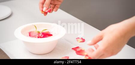 Die weiblichen Hände der Kosmetikerin bereiten das Maniküre-Bad mit Rot und Rosa vor rosenblüten auf dem Tisch im Spa Stockfoto