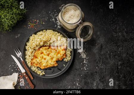 Gegrilltes hawaiianisches Huhn mit Käse, Ananas und gekochtem Reis auf einem schwarzen Teller serviert Stockfoto