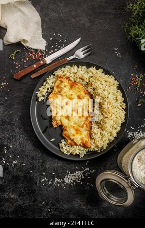 Gegrilltes hawaiianisches Huhn mit Käse, Ananas und gekochtem Reis auf einem schwarzen Teller serviert Stockfoto