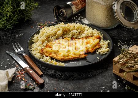 Gegrilltes hawaiianisches Huhn mit Käse, Ananas und gekochtem Reis auf einem schwarzen Teller serviert Stockfoto