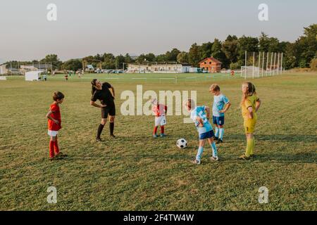 Kinder wärmen sich vor dem Training auf. Gruppe von Kindern Stretching zusammen mit ihrer weiblichen Trainer vor dem Fußballspiel im Feld bei Sonnenuntergang. Stockfoto