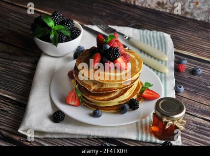 Pfannkuchen mit verschiedenen Beeren auf dunklem Hintergrund. Pfannkuchen stapeln mit Heidelbeeren, Brombeeren, Erdbeeren. Nahaufnahme Stockfoto