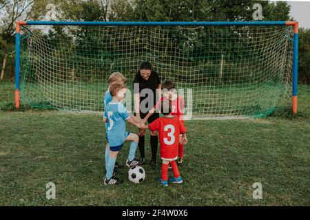 Kinder in Fußballkleider die Hände zusammen zu Beginn des Fußballspiels. Schiedsrichterinnen und eine Gruppe junger Fußballspieler, die um BA stehen Stockfoto