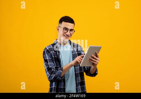 Online-Life-Konzept. Funky junger Mann mit Tablet-pc auf orangen Studio-Hintergrund Stockfoto