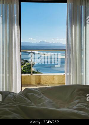 Zimmer mit Blick durch Fenster und Balkongeländer auf Plettenberg Bay, Keurboomsrivier und Indischen Ozean, Südafrika Stockfoto