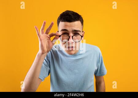 Junge kaukasische Mann in Brille skeptisch, verdächtig aussehen, mit einigen Zweifel auf orangen Studio Hintergrund Stockfoto