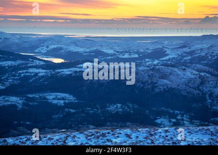 Blick über das Coniston Wasser in Richtung Küste und Walney Offshore Windpark von Red Screes, Lake District, Großbritannien mit leuchtendem Licht bei Sonnenuntergang. Stockfoto