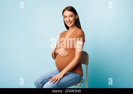 Schwangere Dame Zeigt Geimpften Arm Nach Coronavirus-Impfung, Blauer Hintergrund Stockfoto