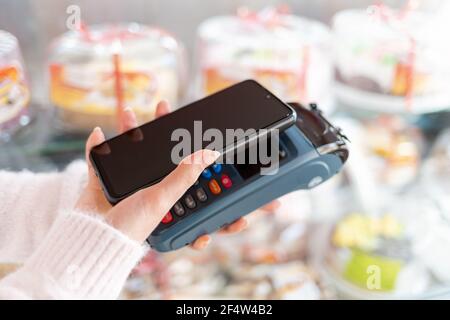 Die Hände einer Frau halten ein Zahlungsterminal und bezahlen für einen Kauf mit einem Smartphone. Speicherplatz kopieren. Das Konzept von NFC, Business und Banking trans Stockfoto