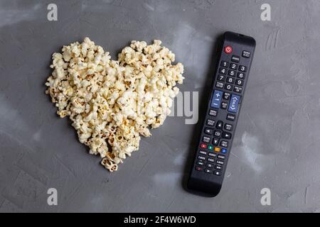 Popcorn in Form eines Herzens und TV-Fernbedienung auf grauem Stein Hintergrund. Liebe Film. Draufsicht. Stockfoto