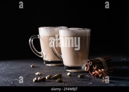 Zwei Tassen Chai Tee Latte, heißer Tee Drink mit geschäumter Milch auf dunkelschwarzem Hintergrund Stockfoto