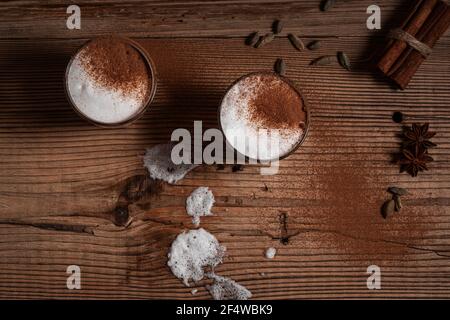 Glas Chai Tee Latte, heiße Latte Schaumgarnierung mit gemahlenem Zimt, Getränk mit geschäumter Milch und Spritzer auf rustikalem Holzhintergrund, Draufsicht Stockfoto