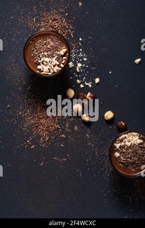 Hausgemachte dunkle Schokolade Mousse mit Haselnüssen in Gläsern auf dunkelgrauen Tisch, Nahaufnahme, Draufsicht Stockfoto