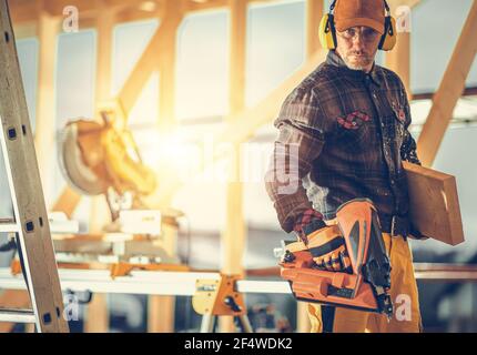 Kaukasischer Bauunternehmer Arbeiter in seinem 40s mit Nagelpistole in der Hand. Tragen einer Schutzbrille und Kopfhörer zur Geräuschreduzierung. Bauart Ind Stockfoto