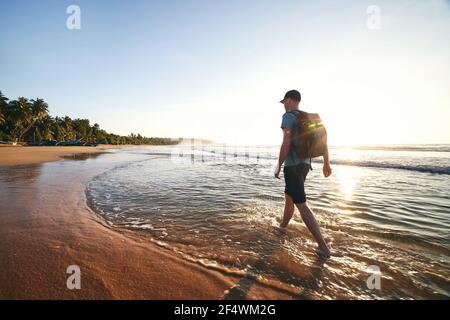 Alleinreisende, die am leeren Strand spazieren. Rückansicht des Mannes mit Rucksack bei Sonnenaufgang. Schöne Sandküste in der Nähe von Tangalle in Sri lanka. Stockfoto