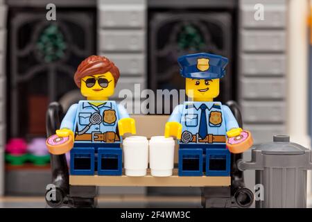 Tambow, Russische Föderation - 19. März 2021 Lego Polizist und Polizistin minifiguren sitzen auf einer Bank und trinken Kaffee und essen Donuts. Stockfoto