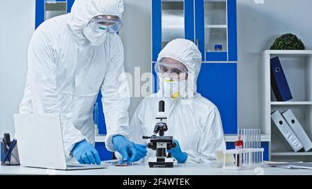 Wissenschaftler in Hazmat Anzug zeigt Blutprobe an Kollegen in der Nähe Mikroskop Stockfoto