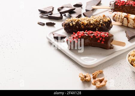Gefrorene Bananenlollipops mit Walnüssen und roten Herzen streut auf weißem Hintergrund. Leckere hausgemachte Süßigkeiten für Kinder. Speicherplatz kopieren. Nahaufnahme. Stockfoto