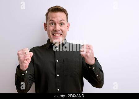 Fröhlich fröhlichen Kerl zeigt gewinnende Geste isoliert auf weißem Studio-Hintergrund. Porträt des Mannes glänzt mit Glück, feiert den Sieg Stockfoto