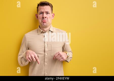 Verärgert Kerl Zeigefinger nach unten, kopieren Raum isoliert gelben Hintergrund, Porträt des Mannes in Freizeitkleidung Blick auf Kamera Stockfoto