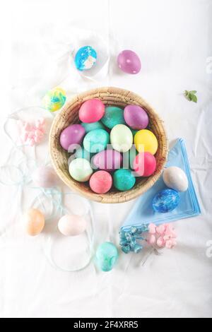 Handbemalte Ostereier in Pastelltönen auf einem mit einer weißen Tischdecke bedeckten Tisch. Draufsicht. Stockfoto