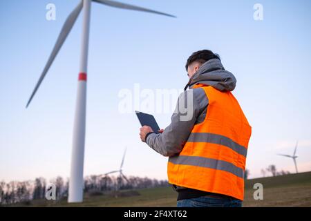 Der Windmühleningenieur führt die Wartung und Reparatur von Windenergieanlagen mithilfe eines Tabletts in der orangefarbenen vesta durch. Stockfoto