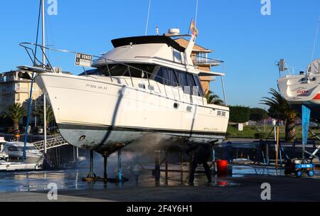 Ein Mann, der mit einer Waschmaschine an der Unterseite einer Motoryacht auf Böcken in der Santander Marina Cantabria Spanien arbeitet Stockfoto