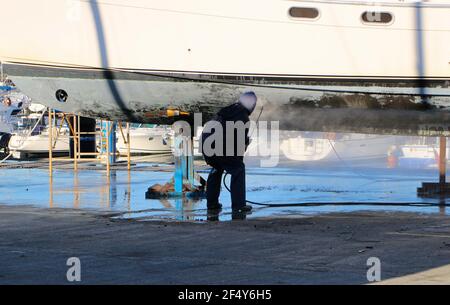 Ein Mann, der mit einer Waschmaschine an der Unterseite einer Motoryacht auf Böcken in der Santander Marina Cantabria Spanien arbeitet Stockfoto