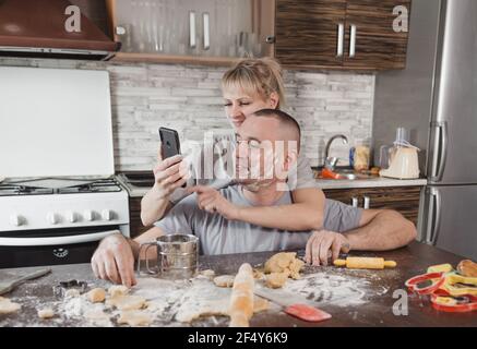 Ein junges glückliches Paar mit Mehl verschmiert nimmt ein Selfie in der Küche. Glücklich und liebevolle Mann und Frau Stockfoto