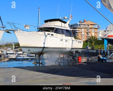 Ein Mann, der mit einer Waschmaschine an der Unterseite einer Motoryacht auf Böcken in der Santander Marina Cantabria Spanien arbeitet Stockfoto