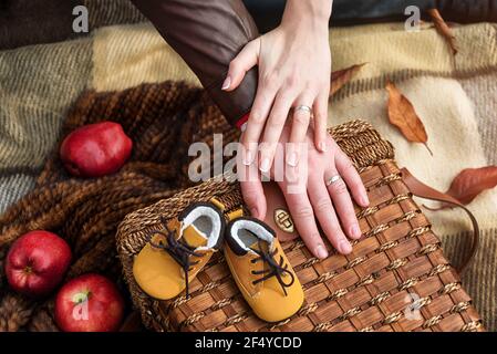 Hände von liebevollen Paar mit niedlichen Baby Schuhe im Herbst Park, Nahaufnahme. Zukünftige Eltern mit neugeborenen Babyschuhen. Geburtserwartung, warten auf Baby. Konz Stockfoto