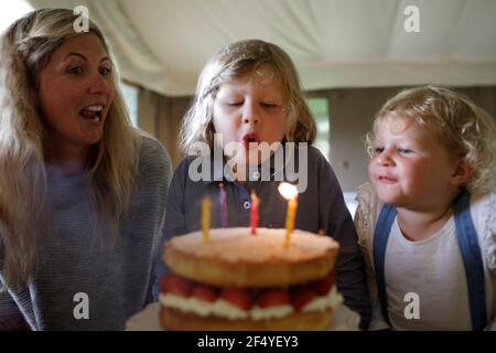 Happy boy bläst Geburtstagskerzen mit Familie Stockfoto