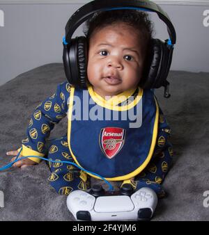 Niedlicher Junge in einem Arsenal Baby Grow posiert mit PS5 Kopfhörern Stockfoto