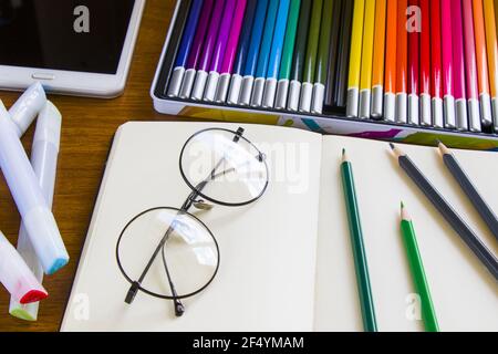 Schreibtisch mit Skizzenstiften und Skizzenbuch, leerem Papier und bunten Bleistiften Stockfoto