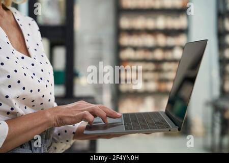 Nahaufnahme der Hände von reifen Geschäftsfrau arbeiten an Der Laptop, während sie in ihrem Töpferwarenladen stand Stockfoto