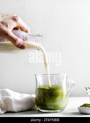 Milch auf pflanzlicher Basis wird mit Matcha Maca Kaffee in ein Glas gegossen. Köstlicher Kaffee/Dessert, der nach dem Frühstück oder am Nachmittag genossen werden kann Stockfoto