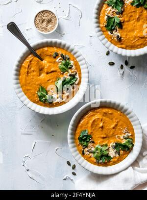 Drei Schüsseln wärmende, beruhigende, supercremige, vegane Currysuppe garniert mit veganem Joghurt, frischen Kräutern, Kürbis und Sesam. Stockfoto