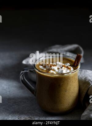 Gemütliche, winterliche Szene - frisch zubereiteter, wärmender, beruhigender veganer Kürbisspice Latte mit Zimtstange, Kokosjoghurt und Kürbisgewürz. Stockfoto