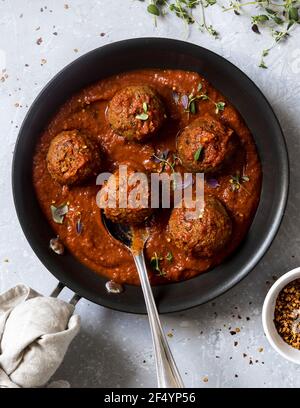 Vegane Dinner-Idee - Tempeh und Tofu-Kugeln in Tomatensauce. Frisch zubereitet, fertig zum Serten auf Tellern. Garniert mit Kräutern und Chilischoten. Stockfoto