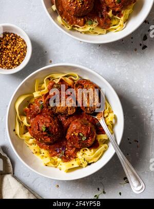 Dinner-Szene - Schüssel mit frisch zubereiteter Pasta mit veganem Tempeh und schwarzen Bohnenkugeln in einer einfachen Tomatensauce mit Chilischoten. Stockfoto