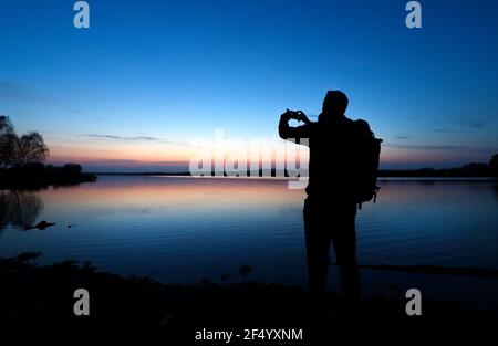 New Forest, Hampshire. 23rd März 2021 UK Wetter. Ein Spaziergänger fotografiert den Sonnenuntergang am Hatchet Pond bei Beaulieu im New Forest. Credit Stuart Martin/Alamy Live News Stockfoto