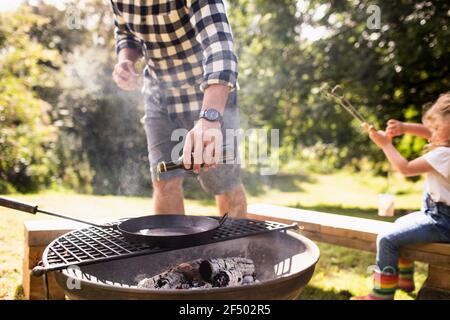 Mann Gießen Olivenöl auf Gusseisen Pfanne auf Hinterhof Grill Stockfoto