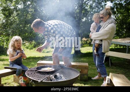 Familie Grillen am Grill im sonnigen Hinterhof Stockfoto