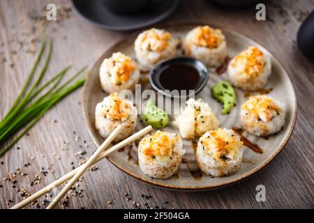 Gebackene Sushi-Maki-Brötchen mit Garnelen und Krabben auf einem Teller mit Essstäbchen, Sojasauce, Wasabi und Ingwer. Japanische traditionelle Fischgerichte aus der Nähe serviert Stockfoto