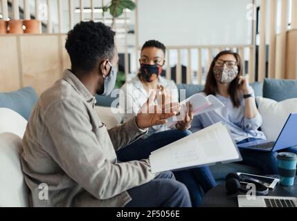 Geschäftsleute in Gesichtsmasken diskutieren Papierkram auf Bürosofa Stockfoto