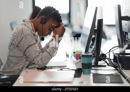 Müde Geschäftsfrau mit Kopf in den Händen am Computer im Büro Stockfoto