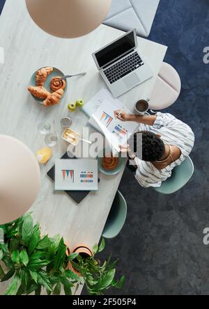 Geschäftsfrau, die beim Frühstück im Büro den Papierkram überprüft Stockfoto