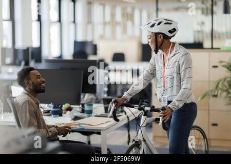 Geschäftsfrau mit Fahrrad im Gespräch mit Geschäftsmann im Büro Stockfoto